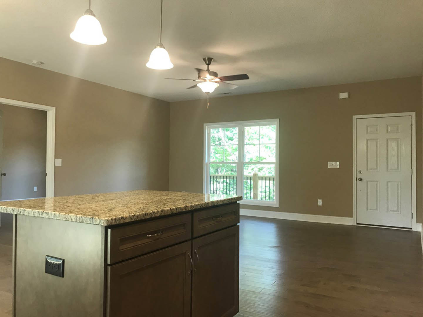 Kitchen with white cabinetry, stone countertop, two ceiling fans with lights, stainless steel hardware, close-up of black electrical outlet, window with metal railing and trees