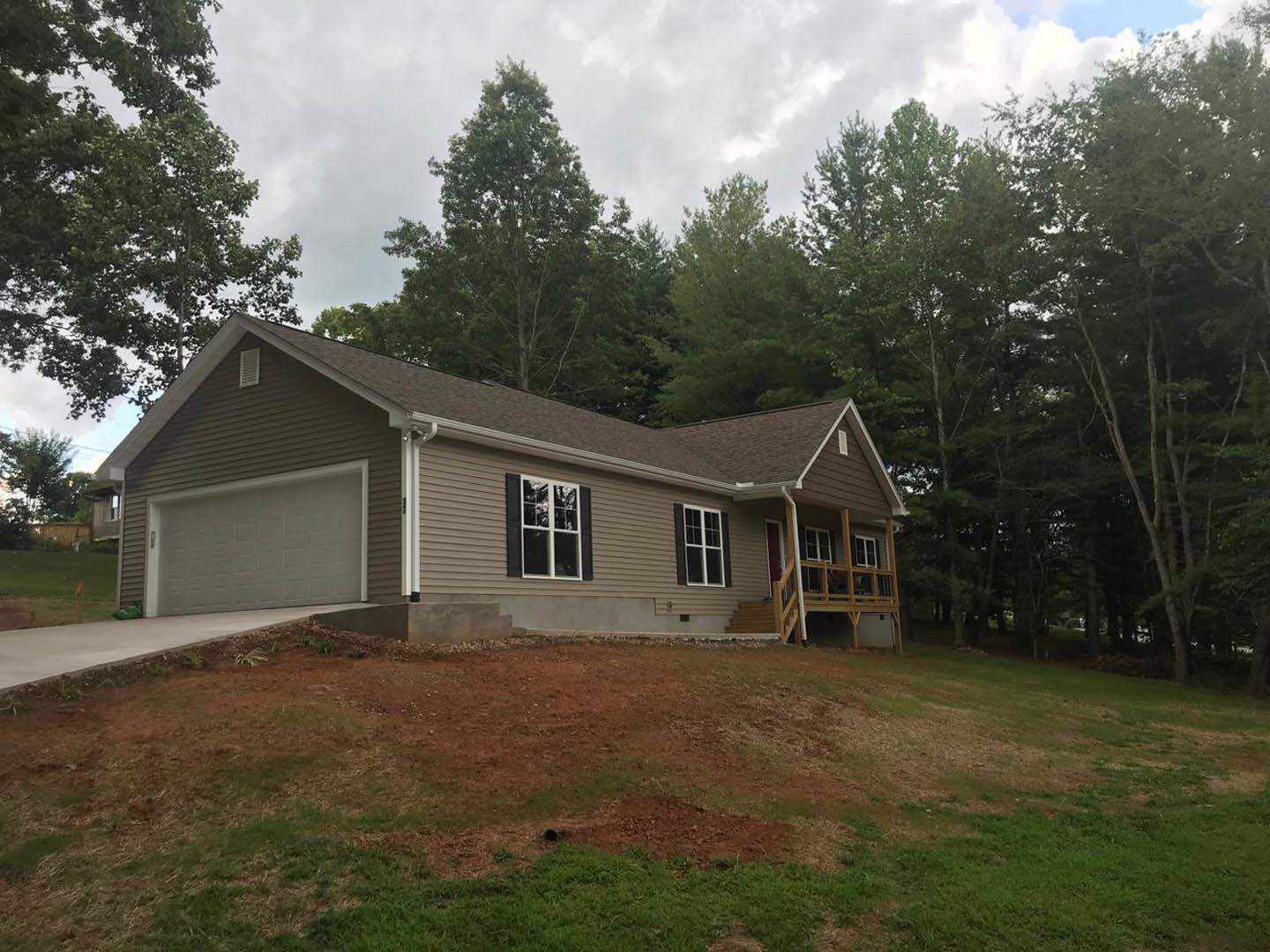 Two-story home with white siding, attached garage, white-framed windows, manicured front lawn, and mature trees under a partly cloudy sky