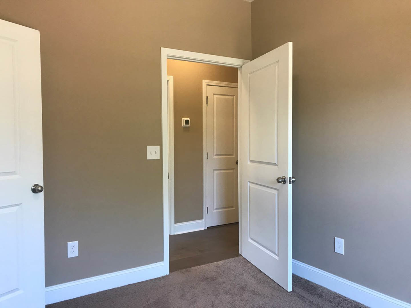 White paneled door with silver handle open against white wall, white door frame, brown carpeted floor, and white light switch on adjacent brown wall