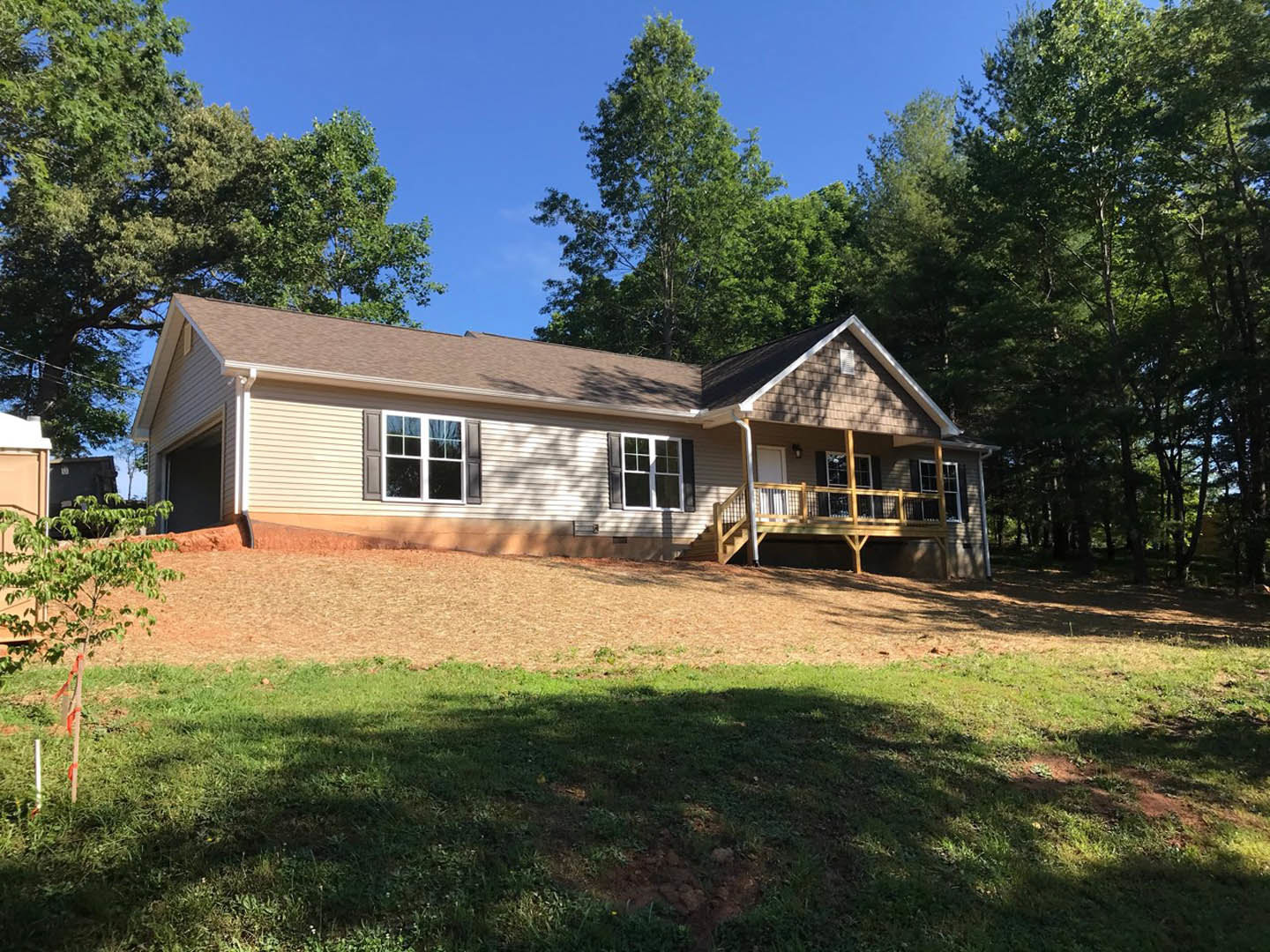White siding house with covered porch, white trimmed windows, green lawn, and tree with red ribbon in front yard