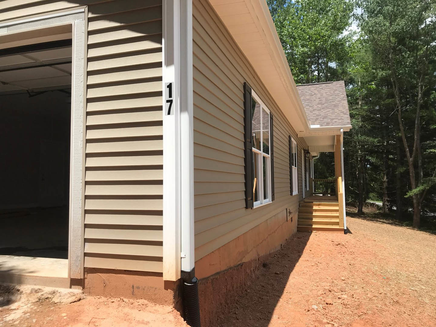 Two-story home with light siding, covered front porch, wooden stairs, open entry door, and large windows; mature tree and shed visible in yard.