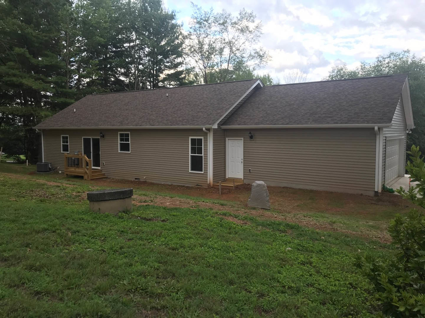 Two-story house with white door and black handle, concrete block foundation, large windows, green lawn, mature trees, and blue sky