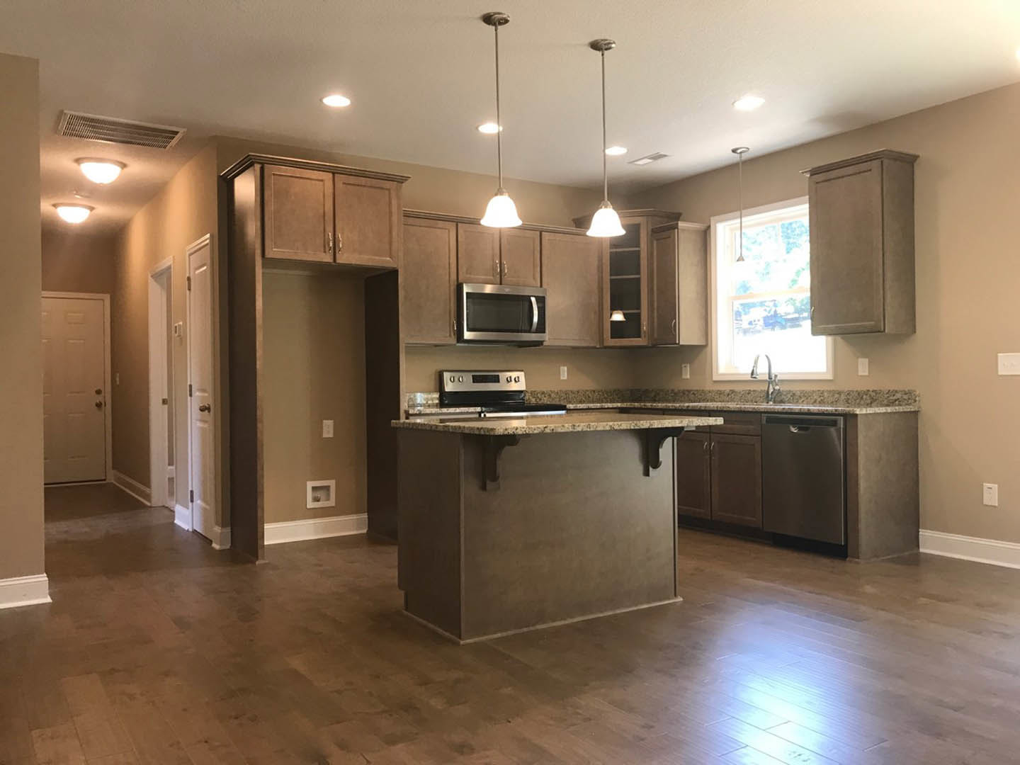Open kitchen with marbled island countertop, wood flooring, white cabinetry, built-in microwave, white door with metal doorknob, and window letting in natural light.