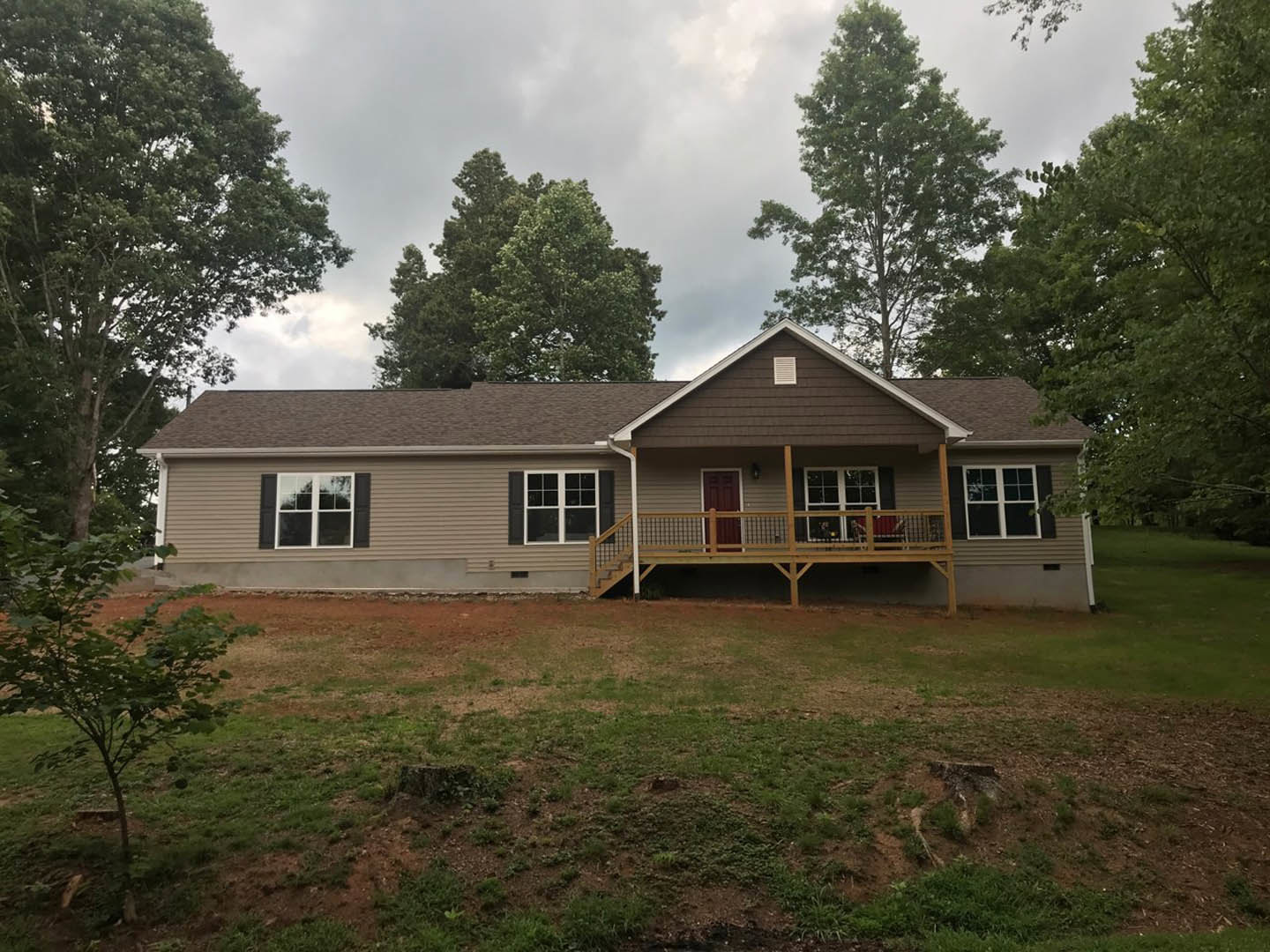 Two-story home with white-framed windows, covered porch, wooden deck, brown fence, and grassy front yard