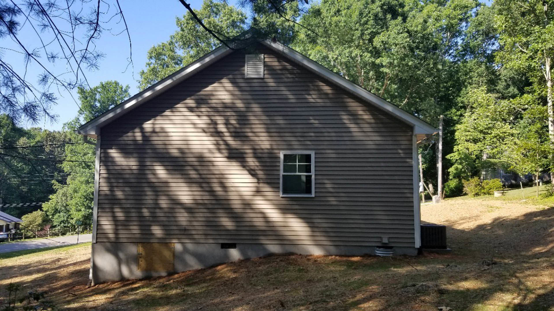 Two-story cottage with white-framed windows, wooden front door with lock, vent and radiator details, surrounded by grass field and mature trees in the background
