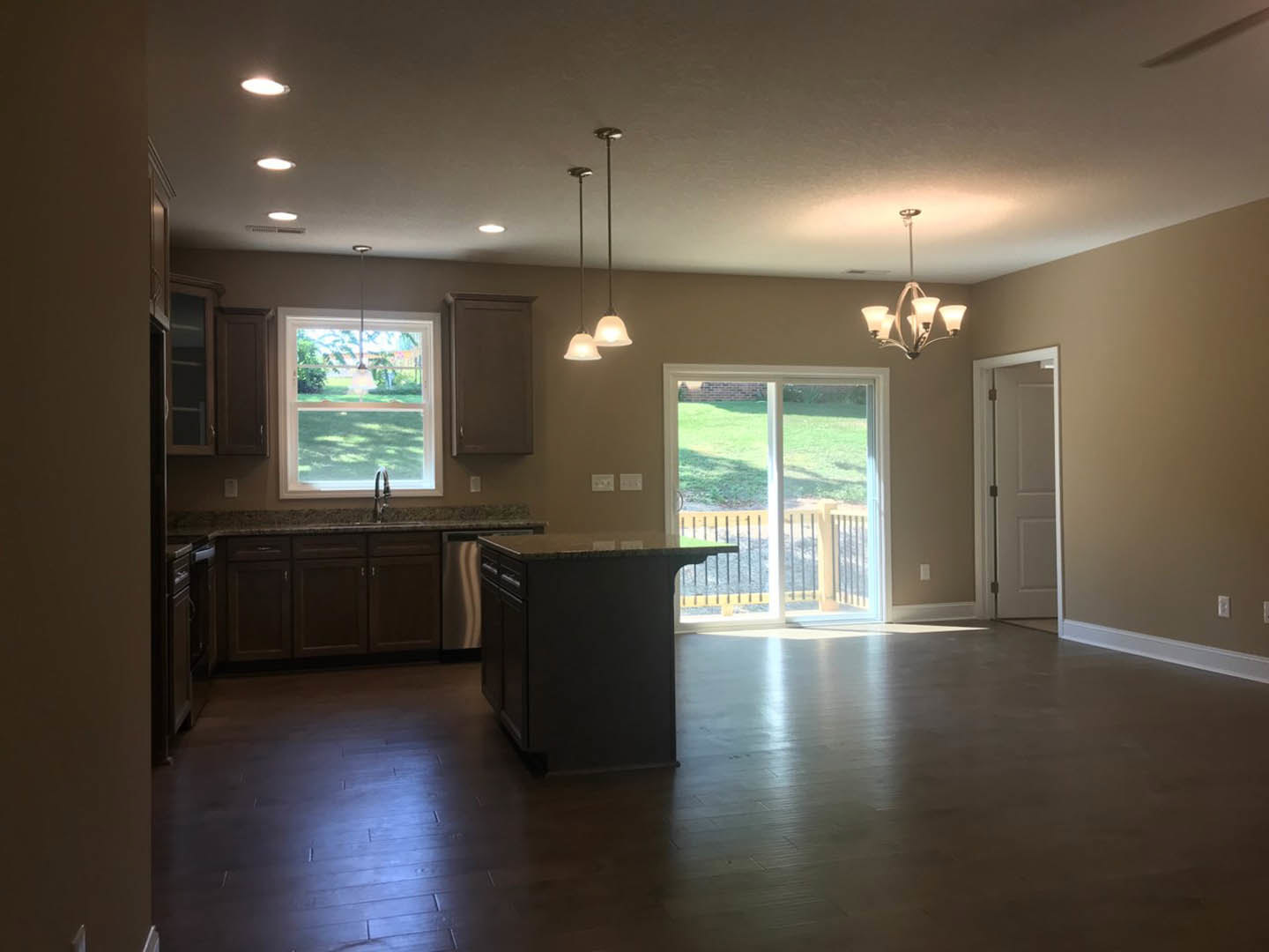 Open kitchen with wood flooring, central island bar with seating, white cabinetry, glass door leading to fenced yard with grass, large window allowing natural light, white interior