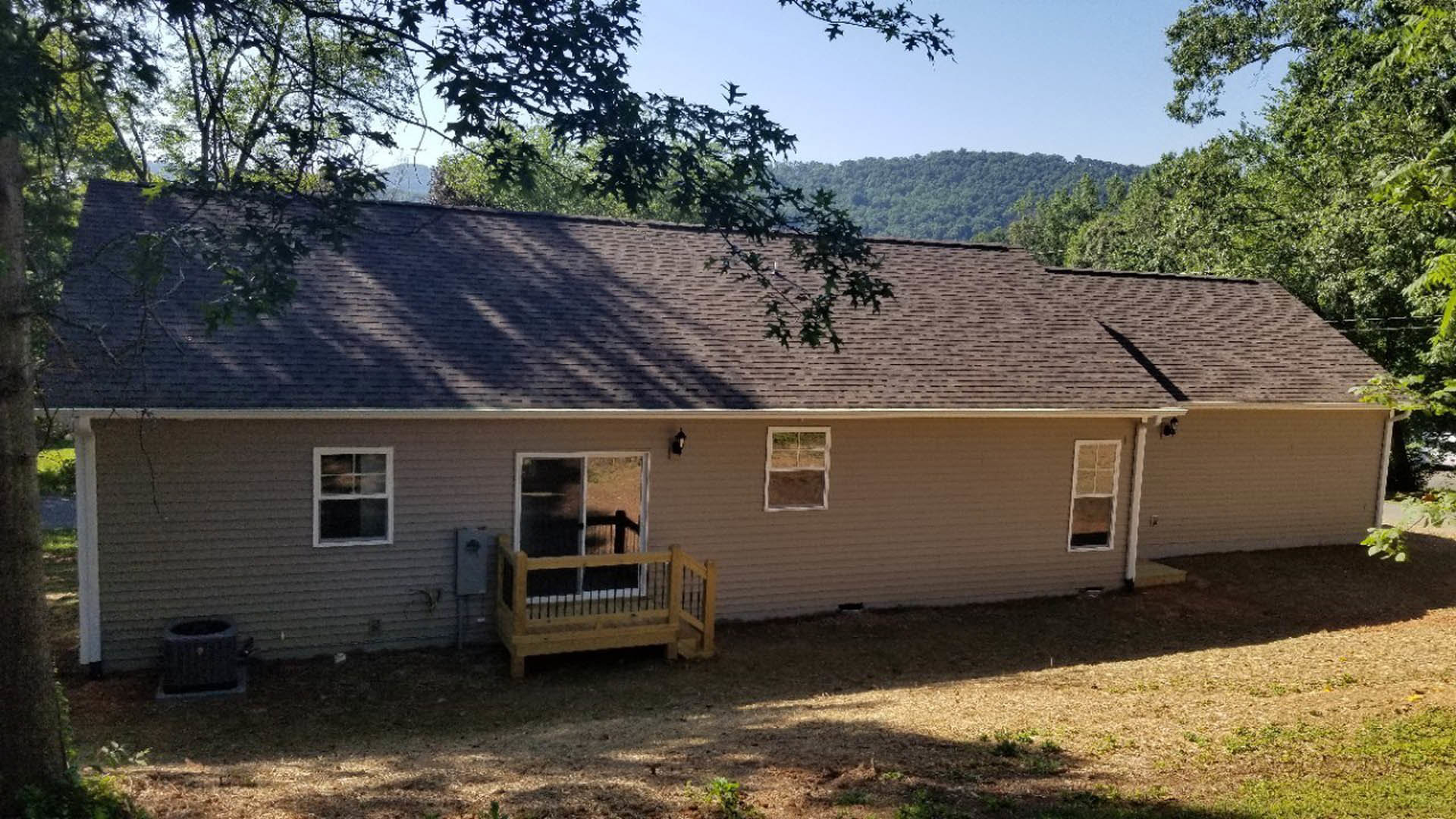 Two-story home with covered front porch, white-framed windows, mature tree in landscaped yard, and dog kennel near exterior wall