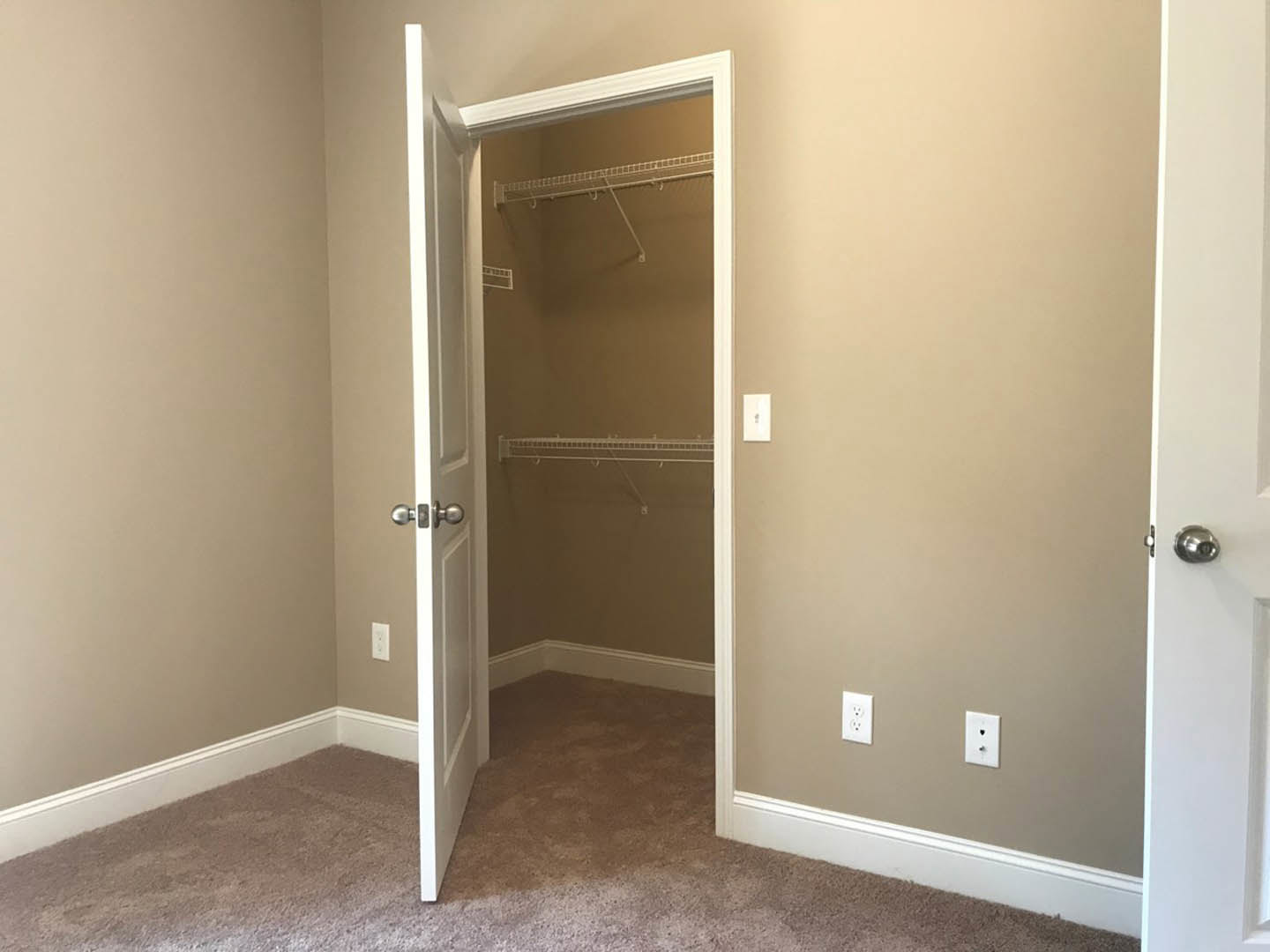 Open closet door with brushed metal knob, white walls featuring a light switch and wall outlet, beige carpeted floor