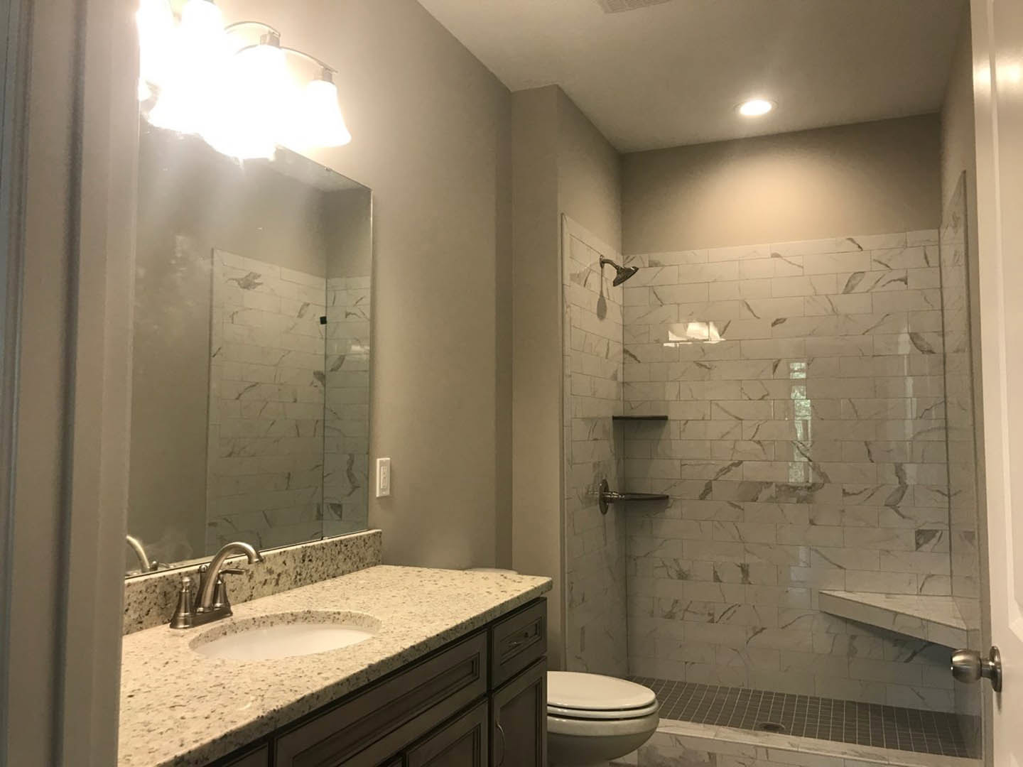 Bathroom with marble countertop, undermount sink, wall-mounted lights, glass-enclosed tile shower, and modern plumbing fixtures