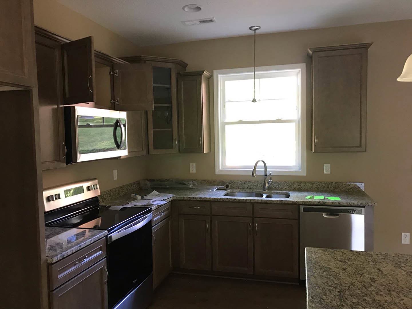 Granite countertops with undermount sink and chrome faucet beneath a window, stainless steel stove and oven, white cabinetry, built-in microwave with glass door, grey interior door