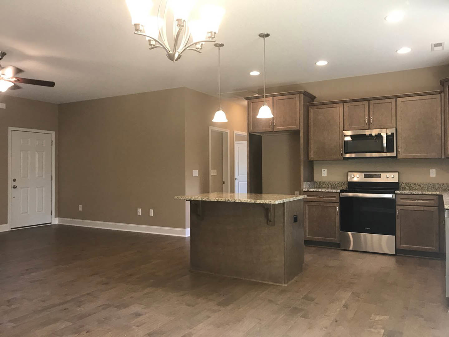 Kitchen with wood flooring, marble island countertop, black and silver oven, white door with silver handle, cabinetry, and modern light fixture