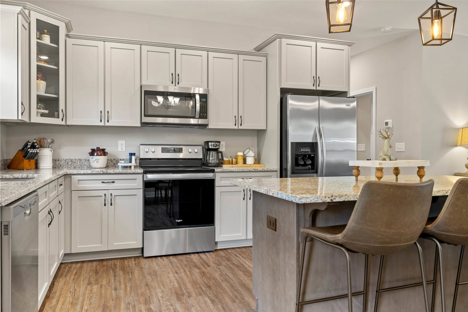 Marble countertop kitchen with stainless steel refrigerator, stove, microwave, cabinetry, sink, chair at counter, and modern light fixture