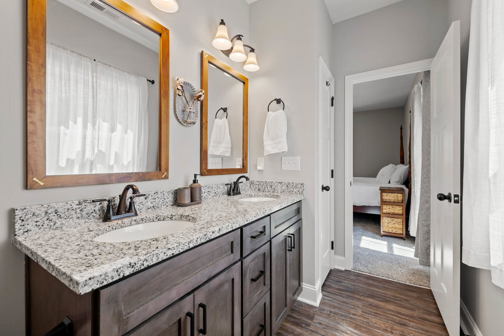 Bathroom with double sinks set in a light stone countertop, two rectangular mirrors above each sink, white towels on black towel holders, white cabinetry below, and neutral tile