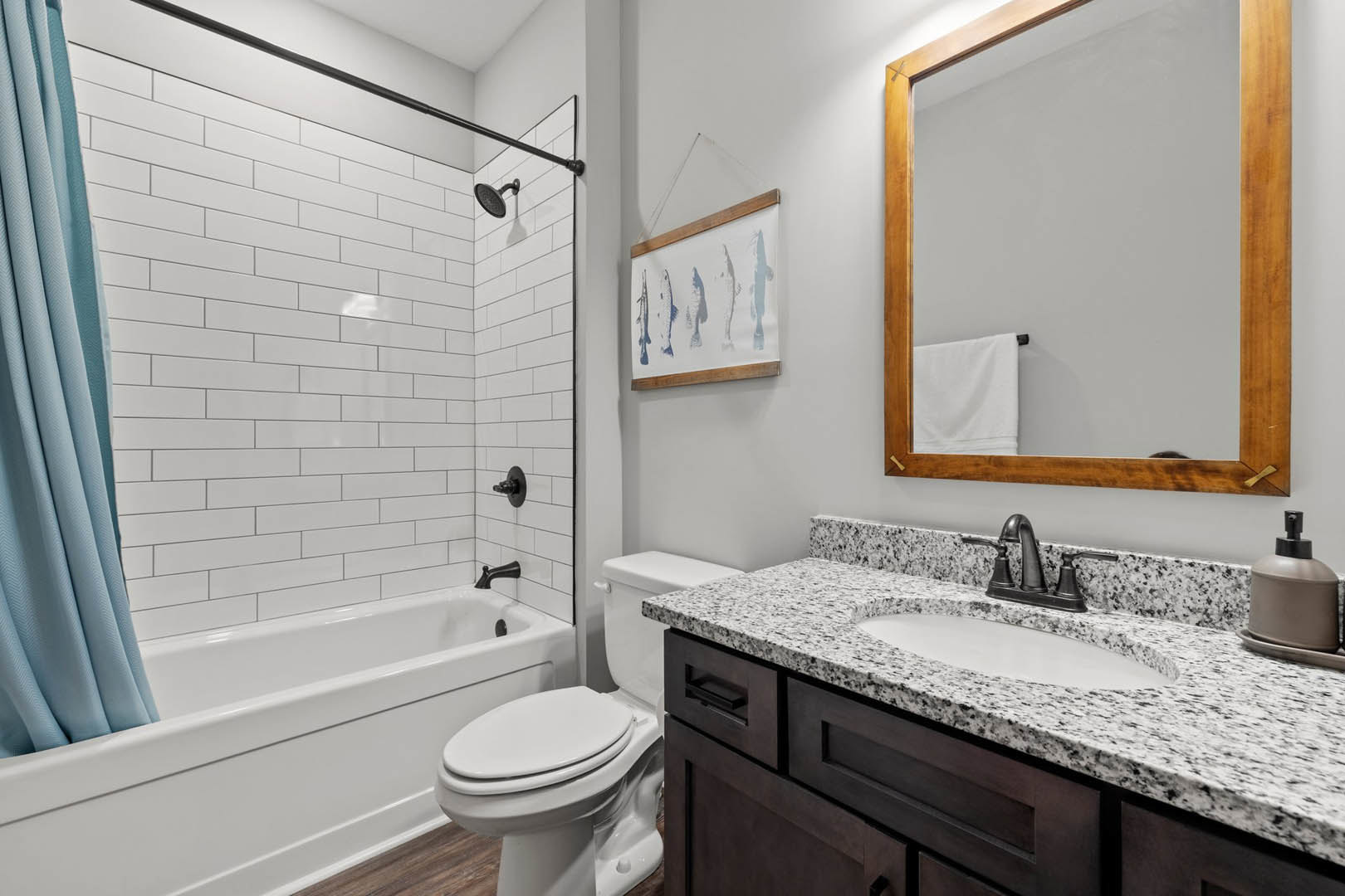 Bathroom with white tile walls, freestanding bathtub, modern sink on stone countertop, wall-mounted mirror above, chrome faucet, towel rack with folded white towel, blue curtain