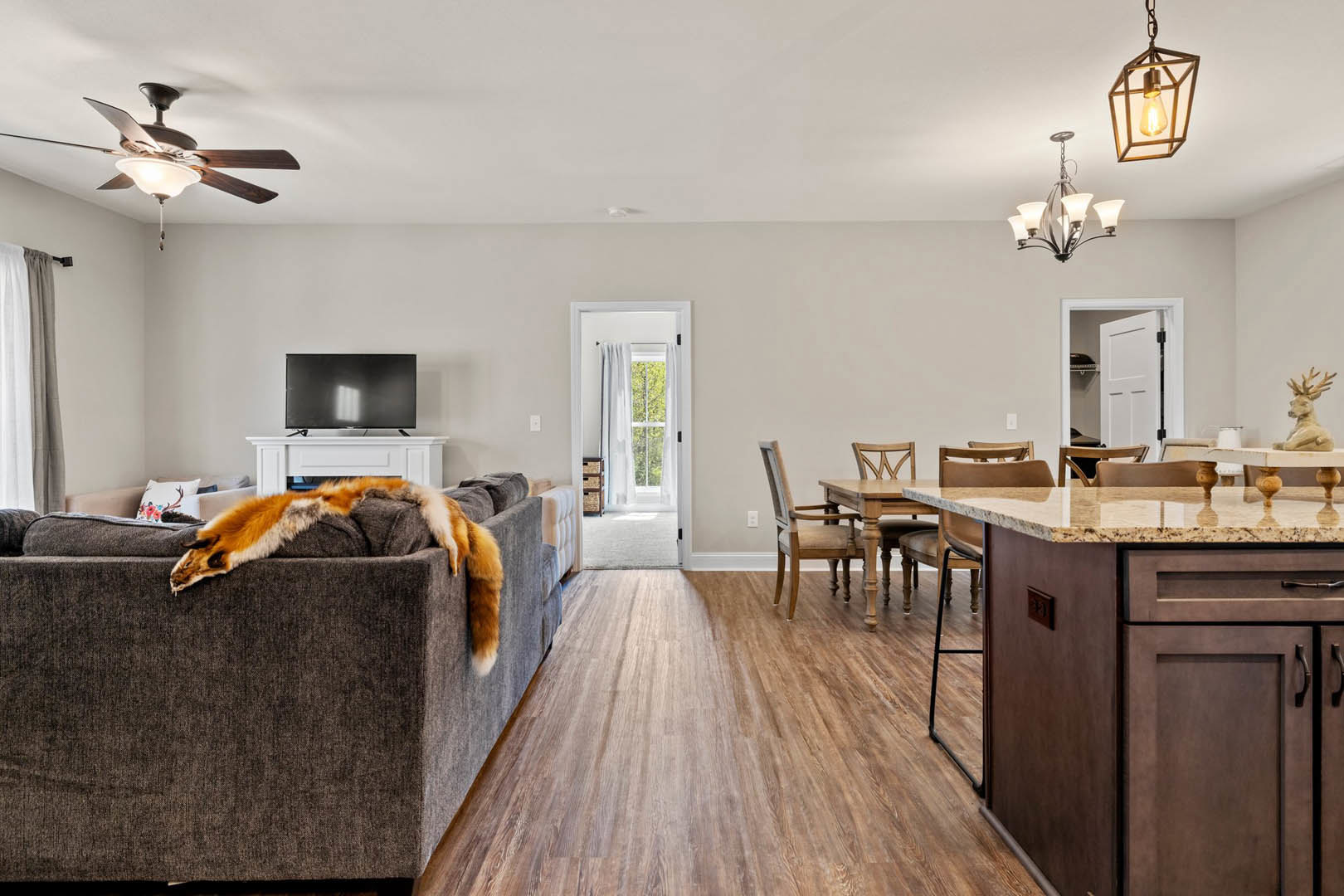 Open concept living room with gray upholstered couch, adjacent kitchen featuring white cabinetry, stone countertops, stainless steel sink, wood flooring, ceiling fan with light