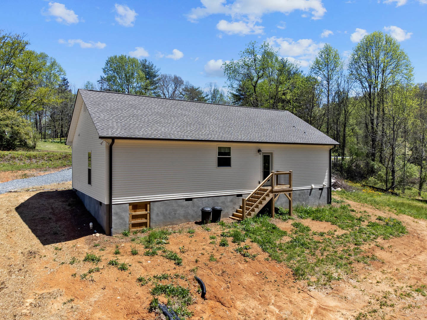 Two-story house with exterior wooden staircase at the back, white-framed window, black trash can, and small shed surrounded by trees and cloudy sky