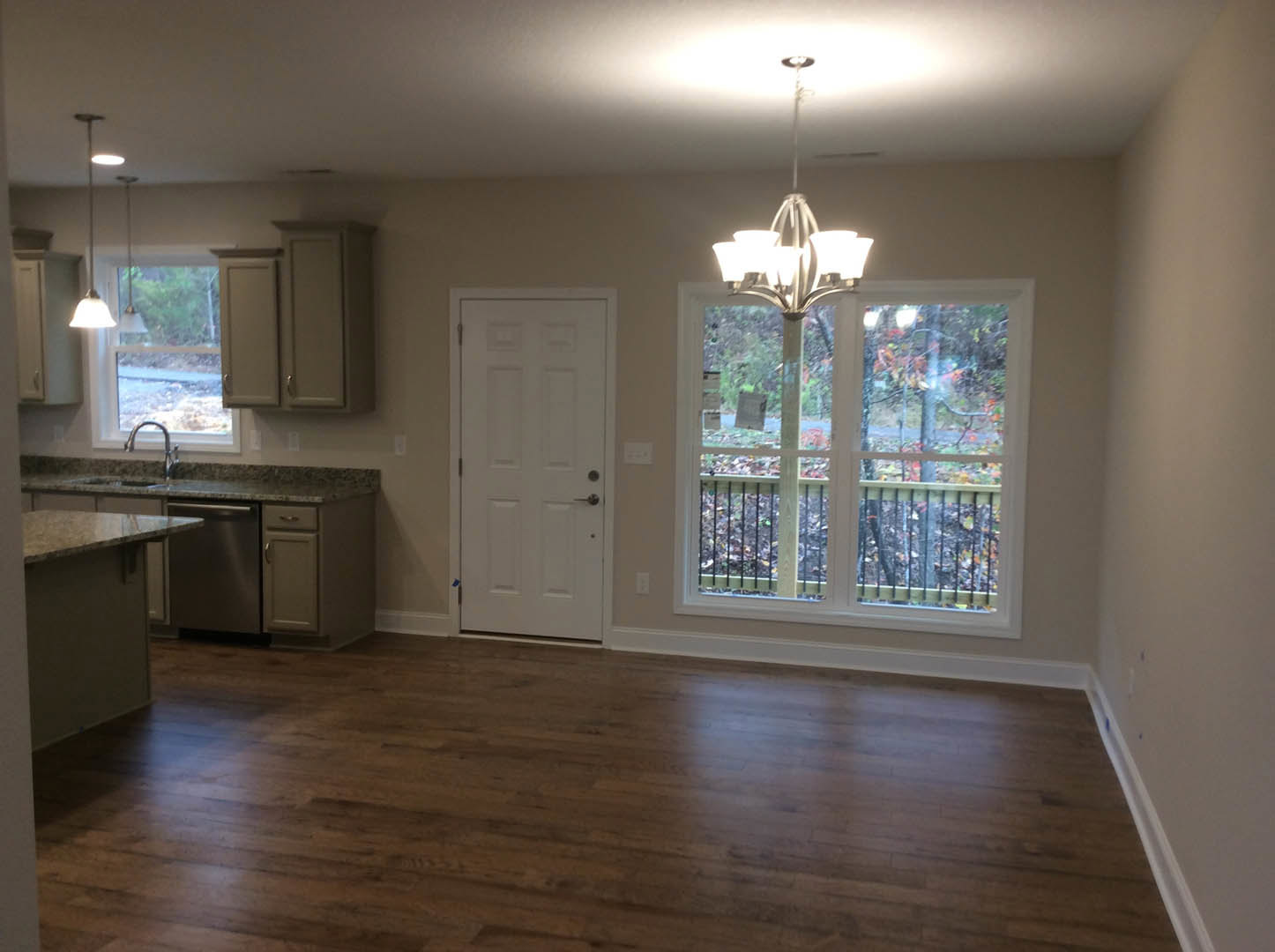 Hardwood floor room with white door, window, and modern light fixture featuring a white shade