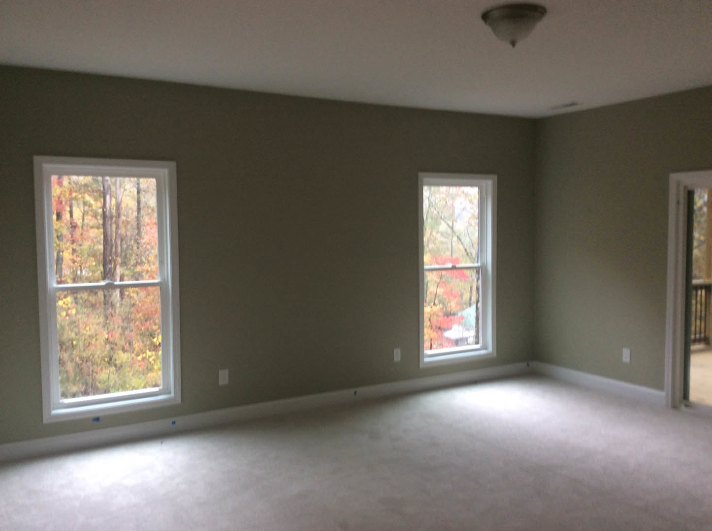 White carpeted room with large windows, white plaster walls, black ceiling border, and outdoor trees visible through the glass.
