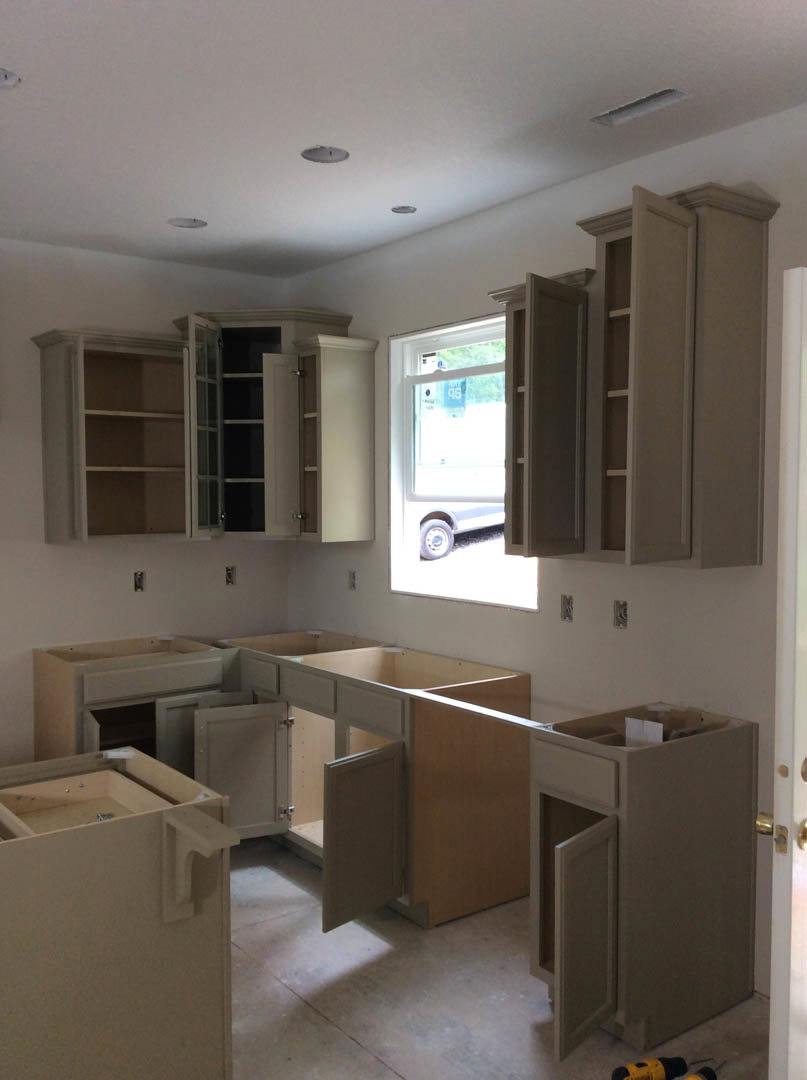 White shaker cabinets and drawers with brushed metal handles, quartz countertop, stainless steel sink, window with a sign, light gray walls, and wood flooring