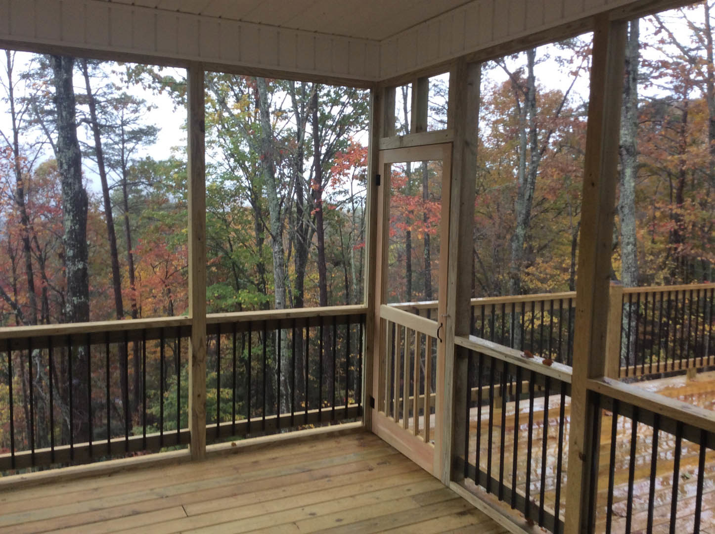 Wood deck porch with metal baluster railing, surrounded by trees, large windows framing outdoor views