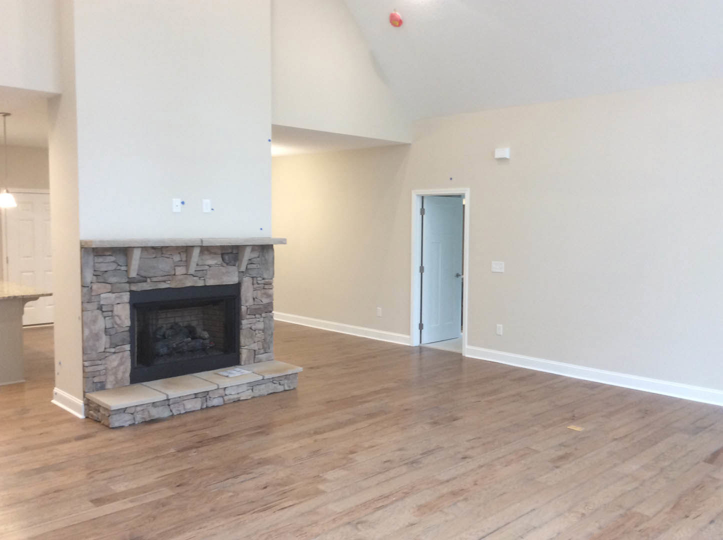 Stone fireplace set in a textured accent wall, wood flooring throughout, white door with silver handle, neutral walls and ceiling.