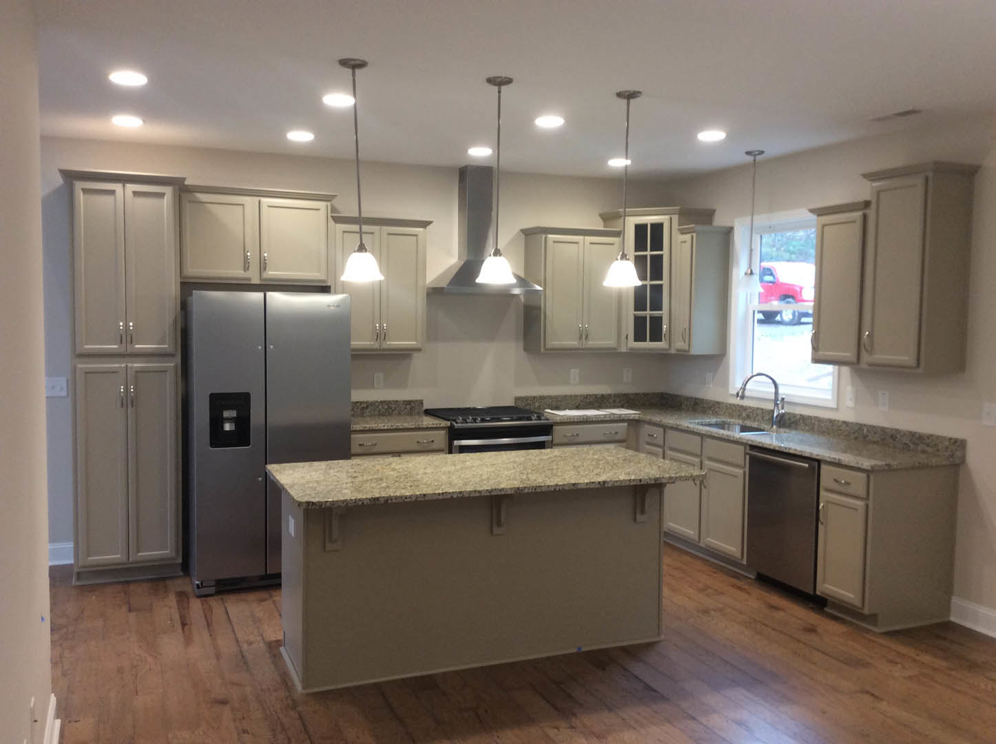 Spacious kitchen featuring a large central island with stone countertop, stainless steel refrigerator, modern cabinetry, tile backsplash, built-in stove, and overhead lighting on a