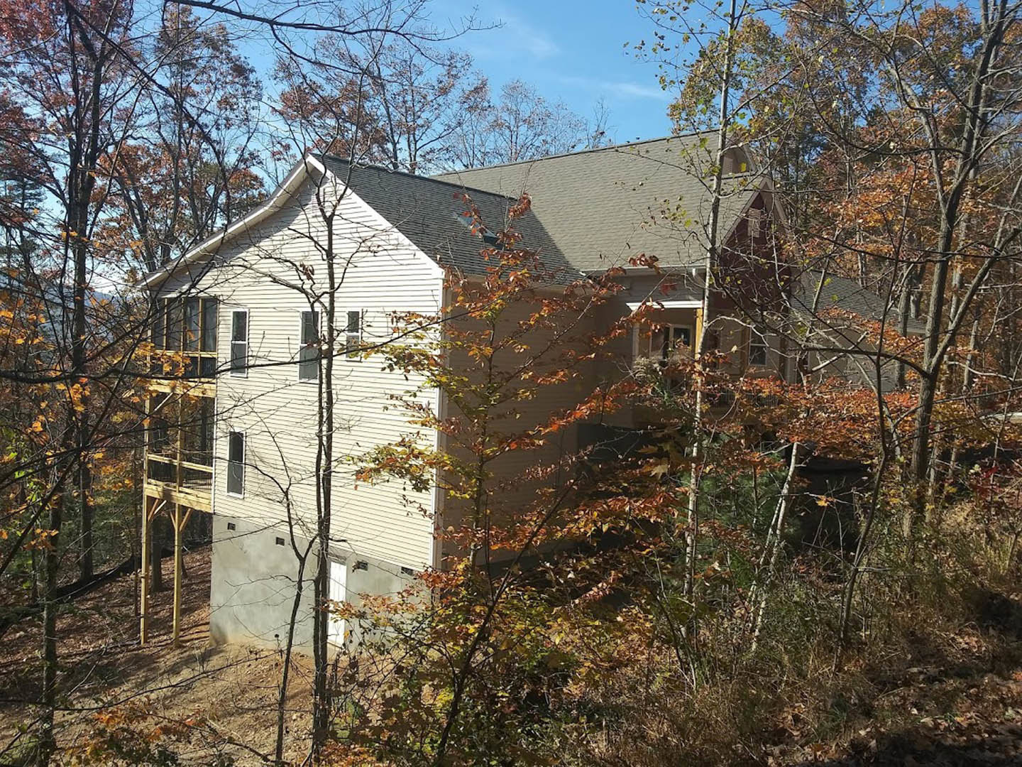 Two-story cottage with large windows, wood siding, and spacious deck surrounded by mature trees with autumn foliage