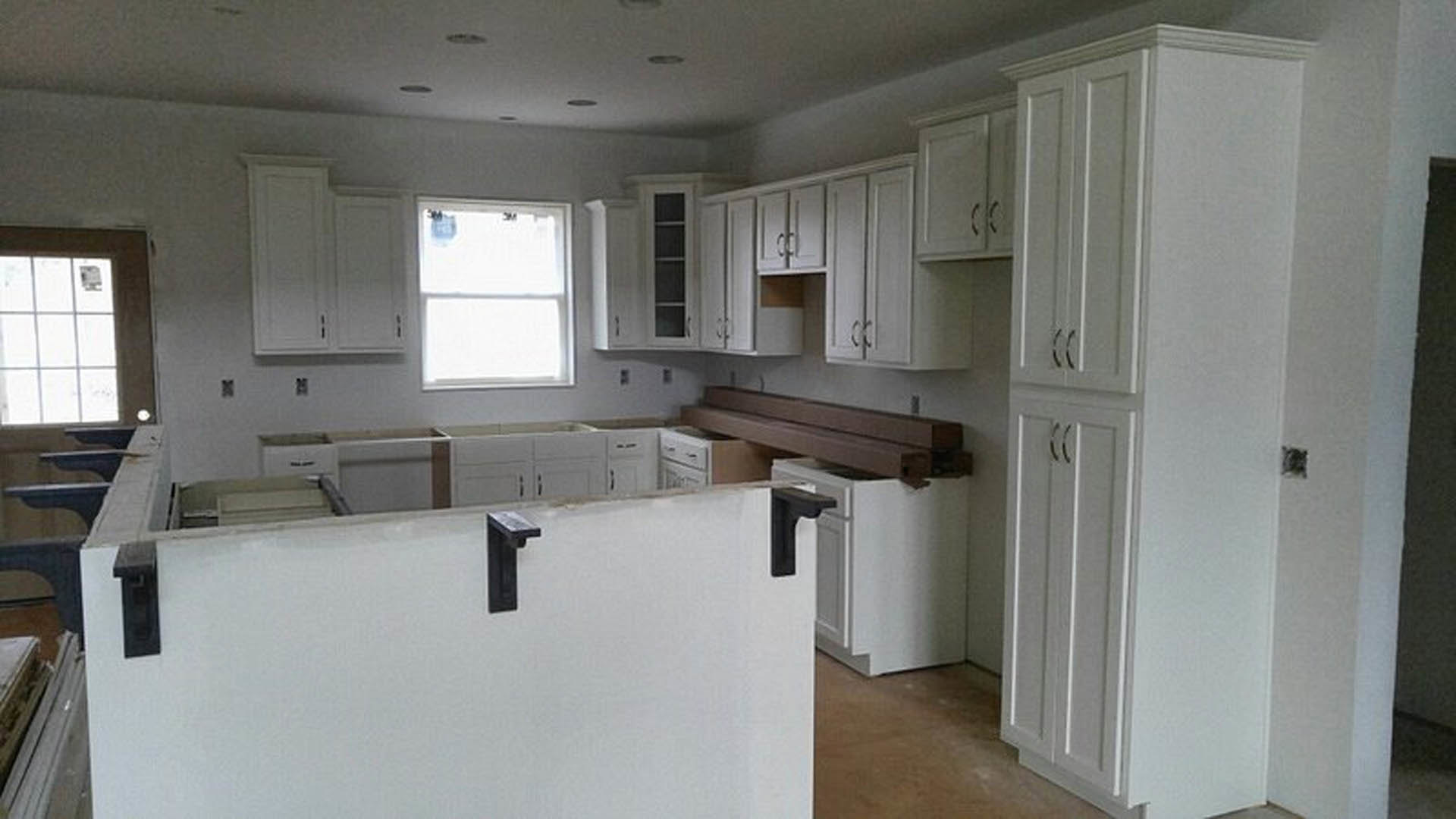 White kitchen cabinets with black metal handles, white countertops, stainless steel sink, and a window above the workspace.