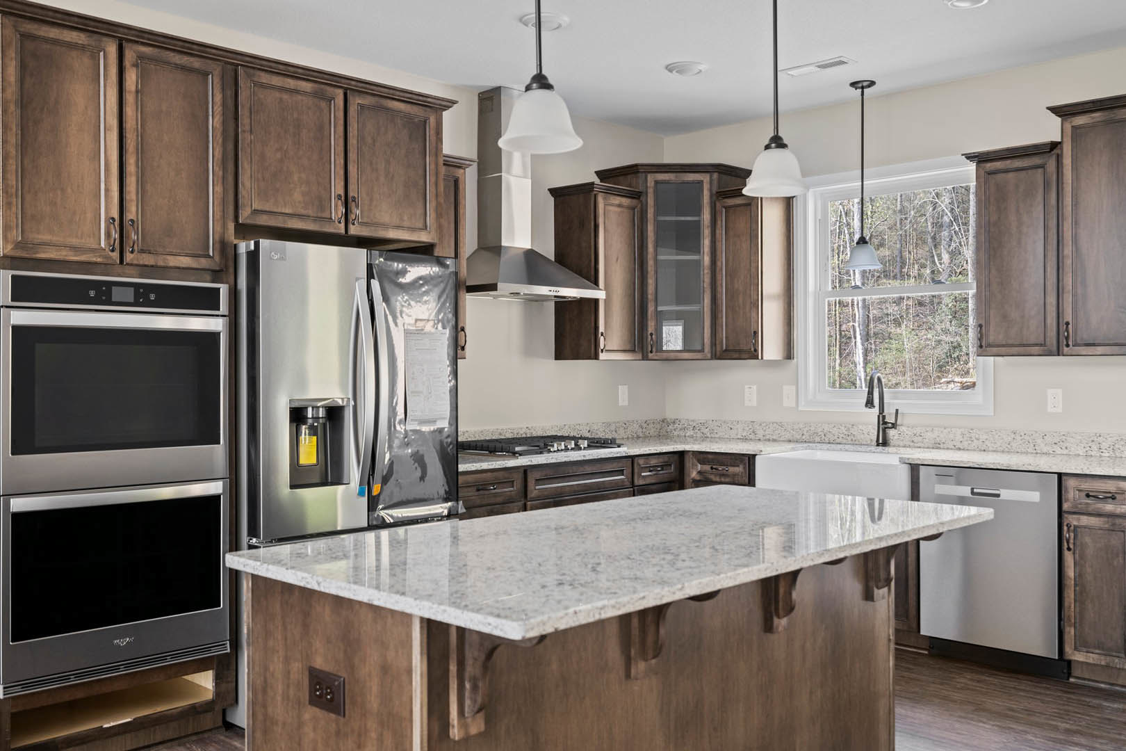Spacious kitchen featuring a large central island with quartz countertop, stainless steel refrigerator and microwave, white cabinetry, modern sink, and a window allowing natural