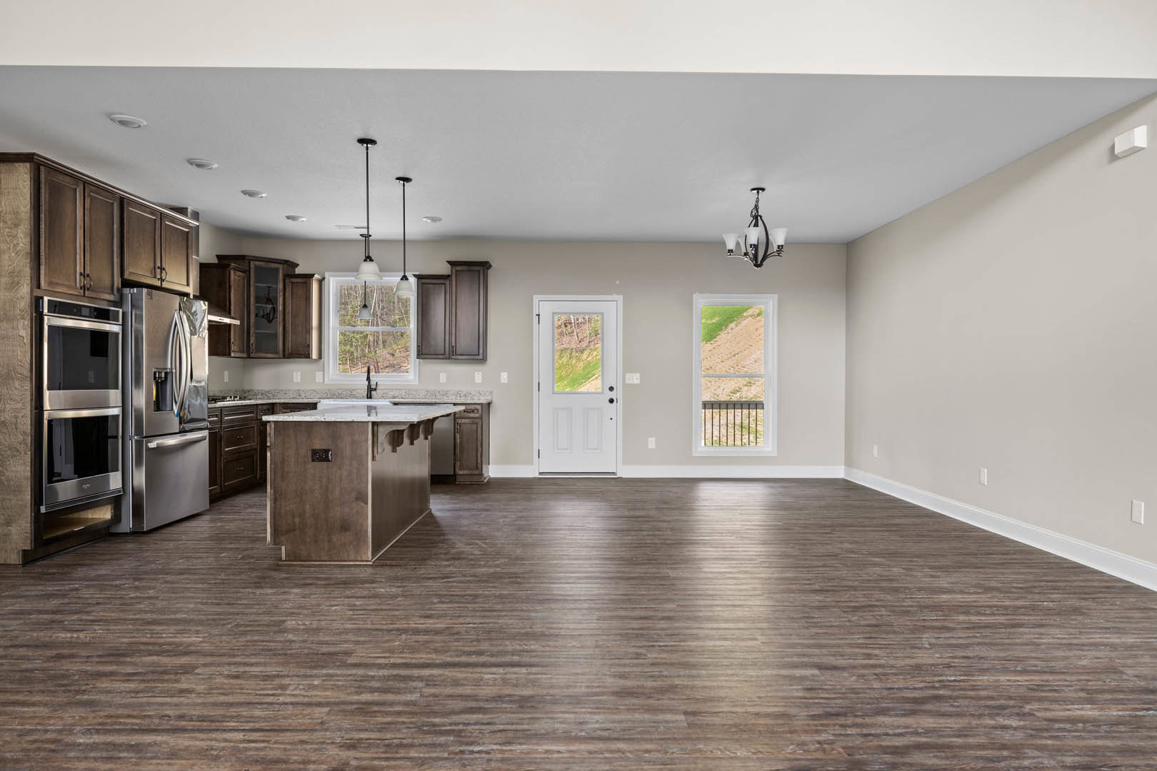Spacious kitchen with wood flooring, white cabinetry, stainless steel refrigerator and microwave, white door with window, view of dirt field through window