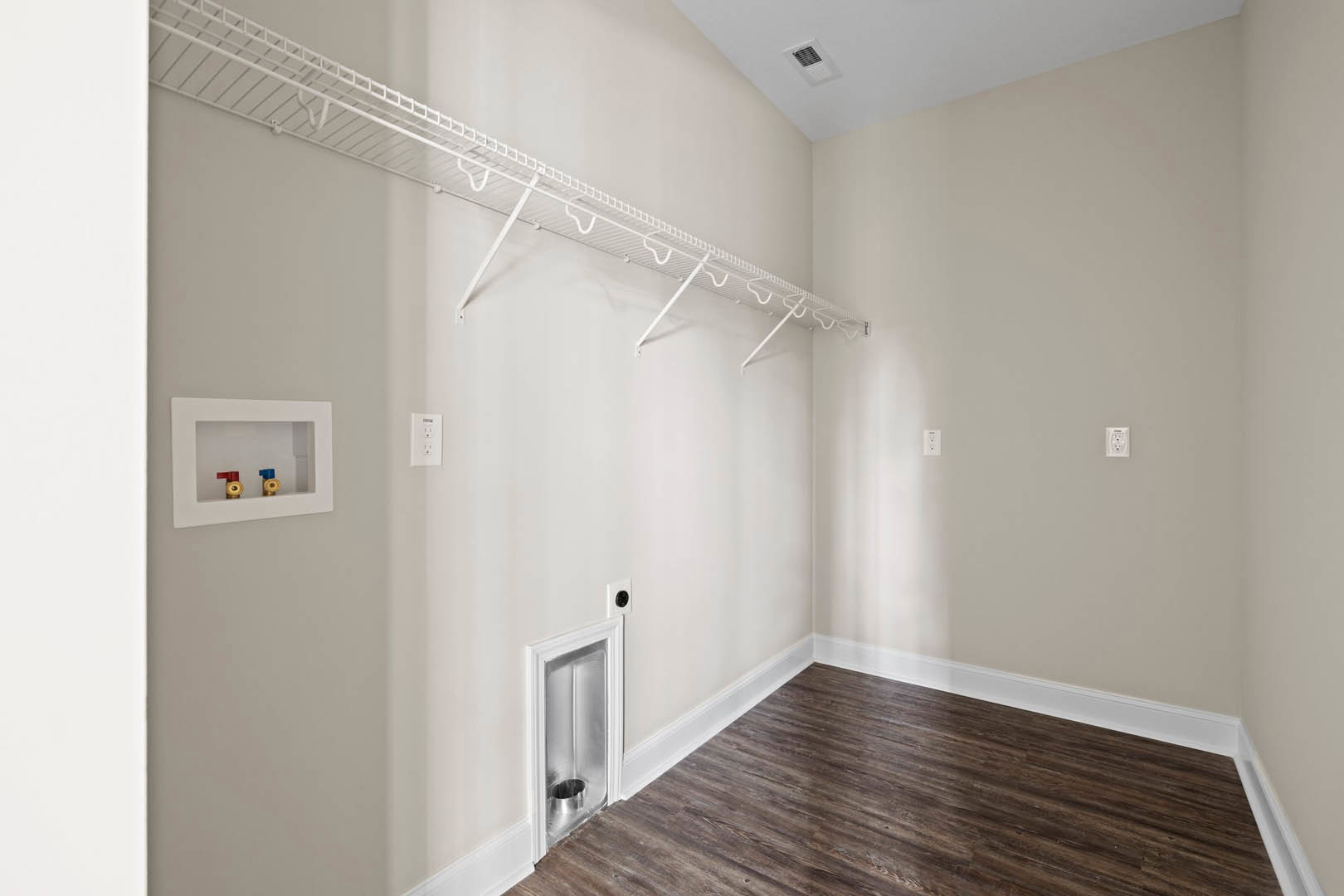Wood flooring with white baseboards, white wall-mounted shelf, and window; visible valves and metal fixture near wall opening.