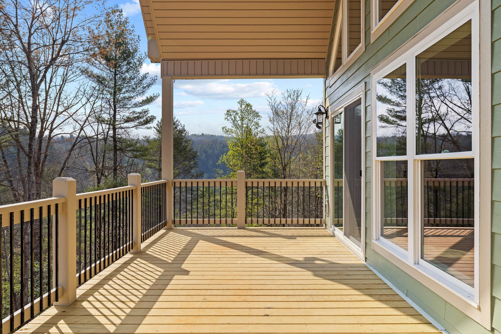 Wooden deck with metal railing, large window on house exterior, trees and sky in background