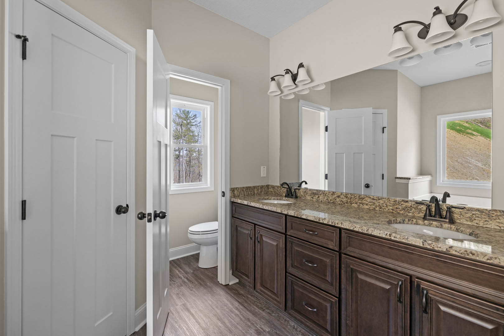 Bathroom with marble countertop, white toilet, white cabinetry, tile flooring, window showing trees and dirt road, modern light fixture