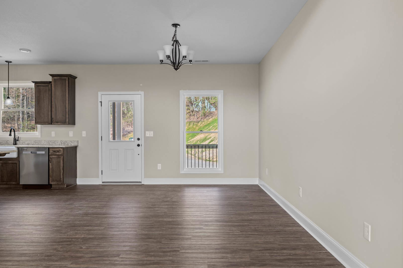 Wood floor with white walls, white door featuring glass window, large window overlooking field and trees, chandelier and lamp fixtures visible.