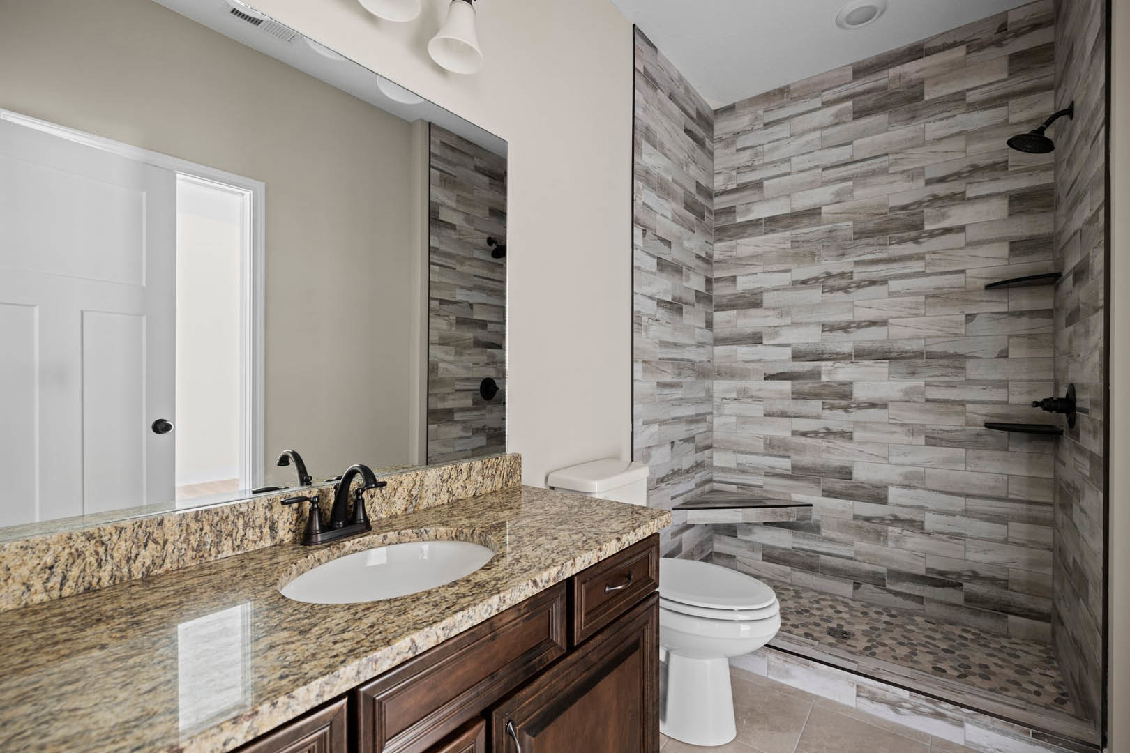 Marble countertop vanity with undermount sink, chrome faucet, glass-enclosed shower, white toilet, white door with black knob, light tile flooring, and neutral wall paint