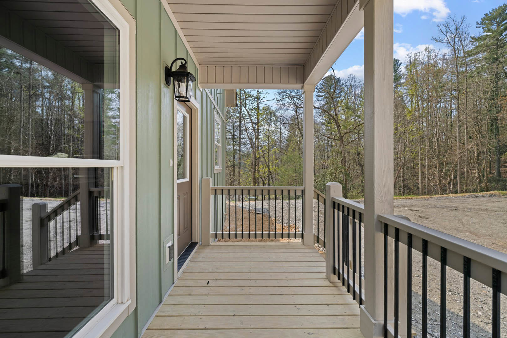 Front porch with black metal railing, wood deck, white ceiling, and hanging lantern next to entry door