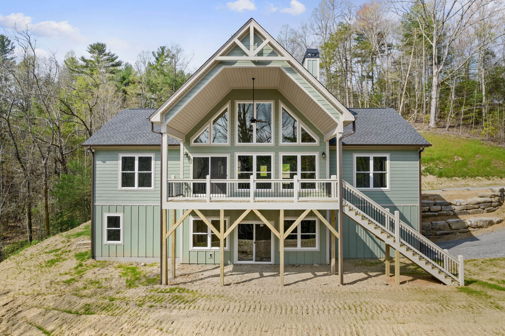 Two-story home with expansive covered porch, white trim, large windows, ceiling fan on porch, exterior staircase, and surrounding landscaping with trees.