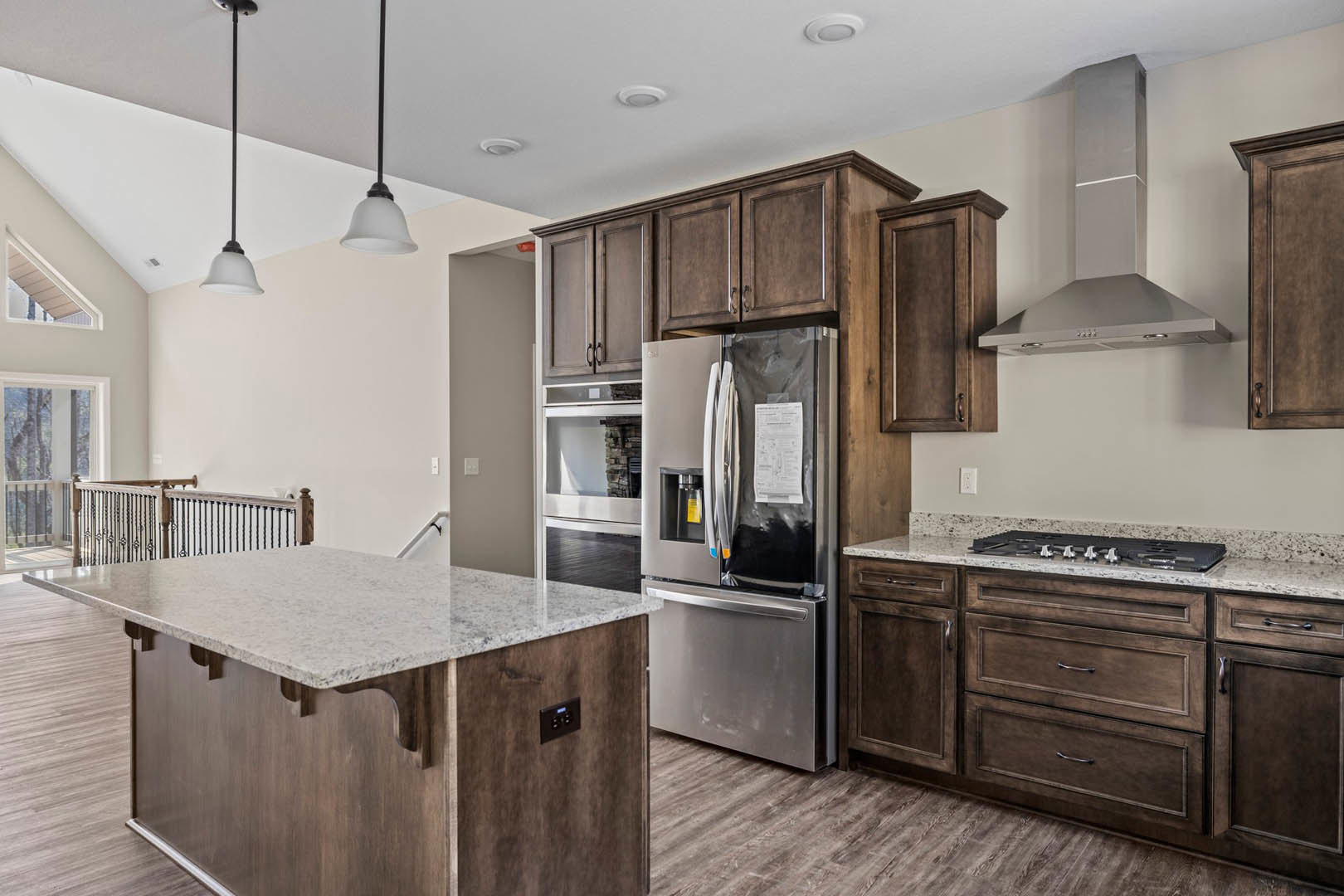 Spacious kitchen featuring a marble-topped island, stainless refrigerator with paper attached, white cabinetry, black electrical outlet with blue indicator light, and sleek black