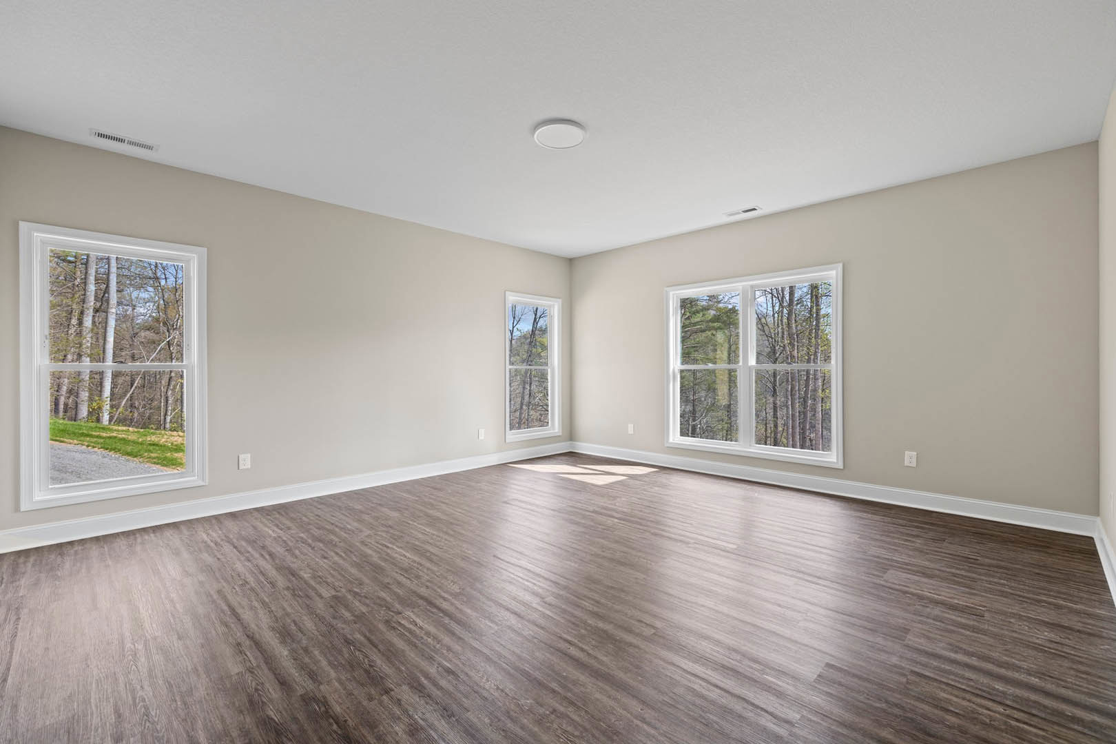 Spacious room featuring wood flooring, large windows overlooking trees and grass, white walls, and a white ceiling with a circular light fixture