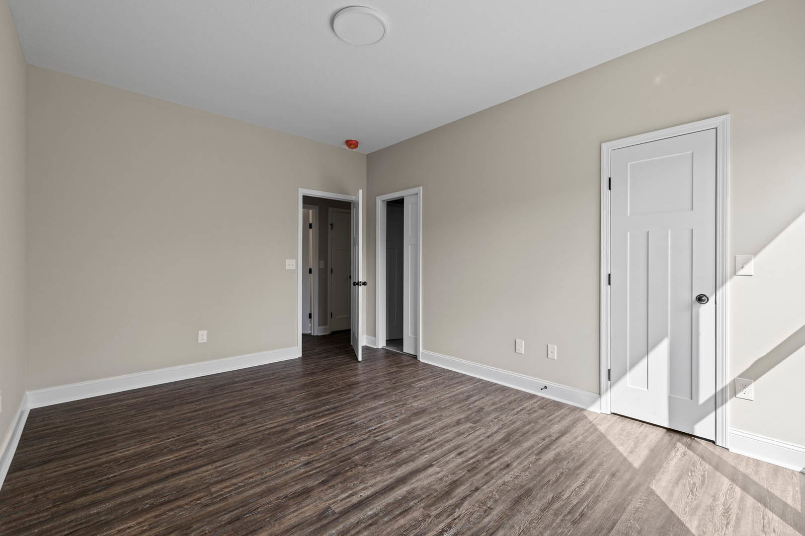 Hallway with white paneled doors featuring black handles, wood flooring, white walls, and white trim