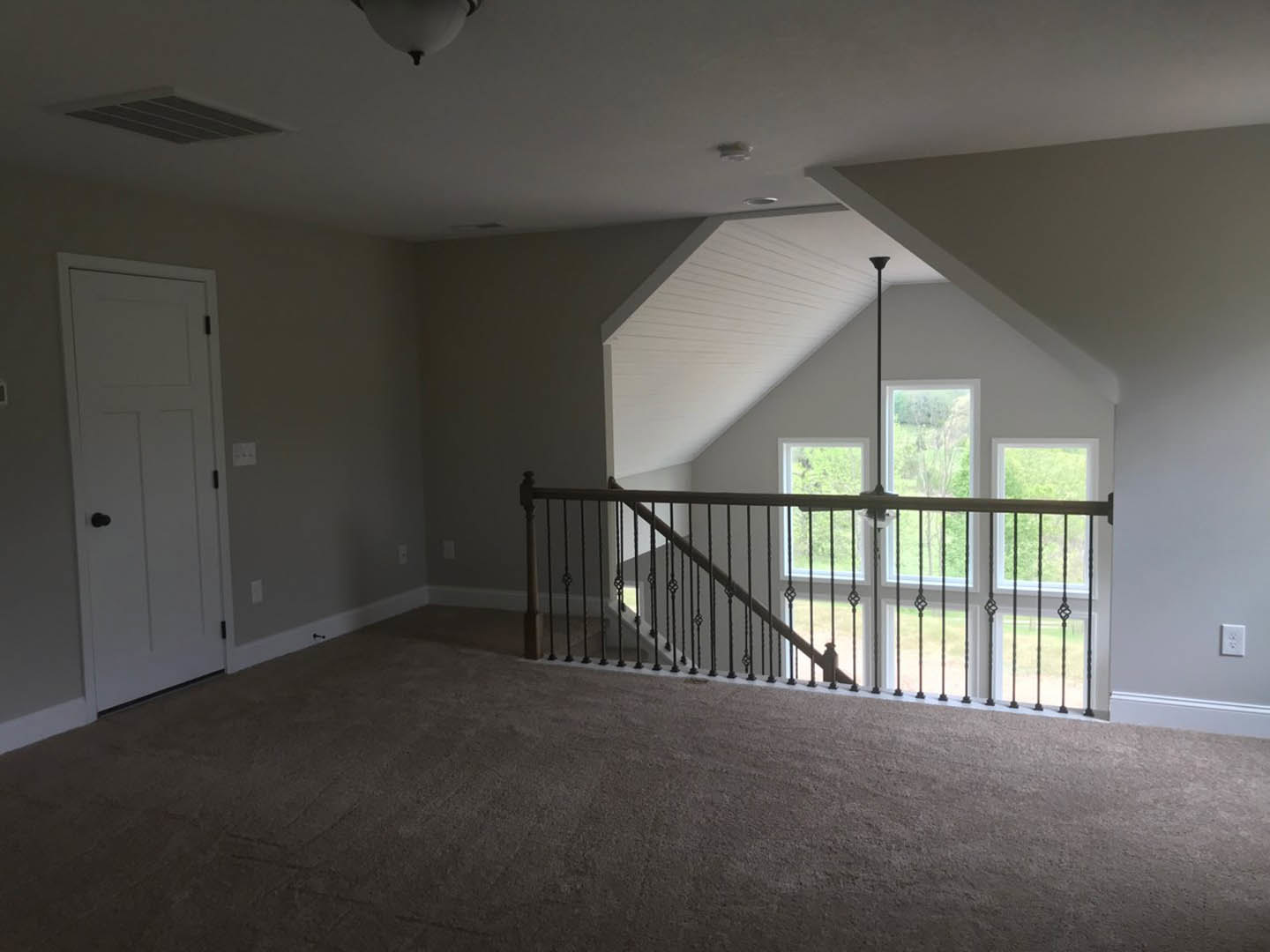 Carpeted room featuring a white staircase with wooden handrail, white paneled door with black knob, smooth plaster walls, and white ceiling