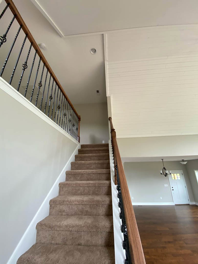 Wood staircase with white balusters and handrail, adjacent to a white door with glass window, wood flooring, and white walls featuring a vertical wooden accent strip