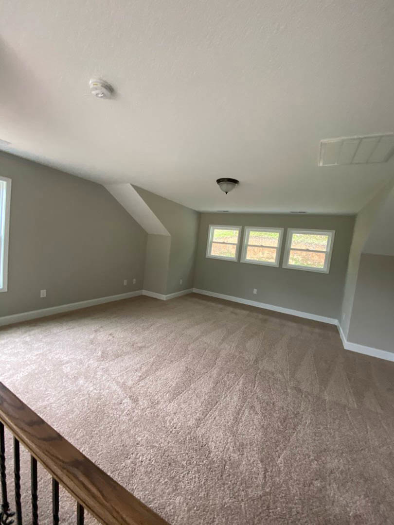 Carpeted room with a row of large windows, white window frames, wooden railing, and white tiled ceiling