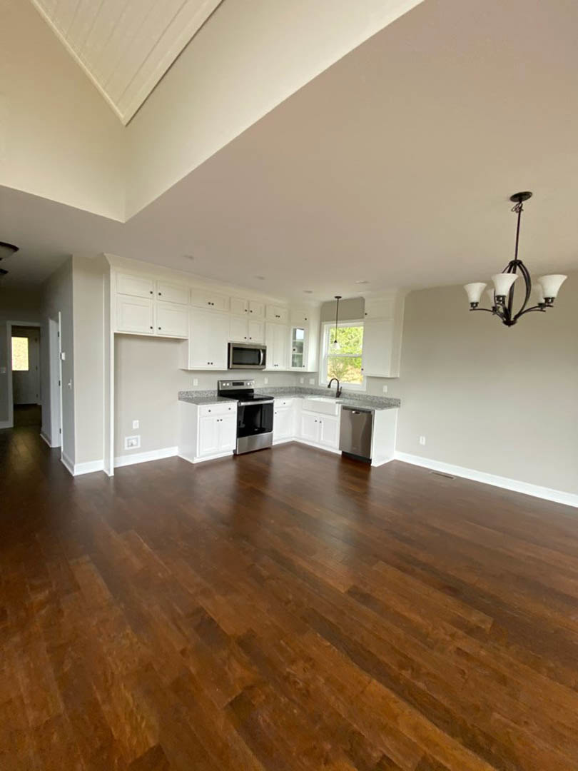 Open-concept kitchen and dining area featuring hardwood floors, white cabinetry, stone countertops, pendant lighting, and a modern chandelier above a wooden dining table.