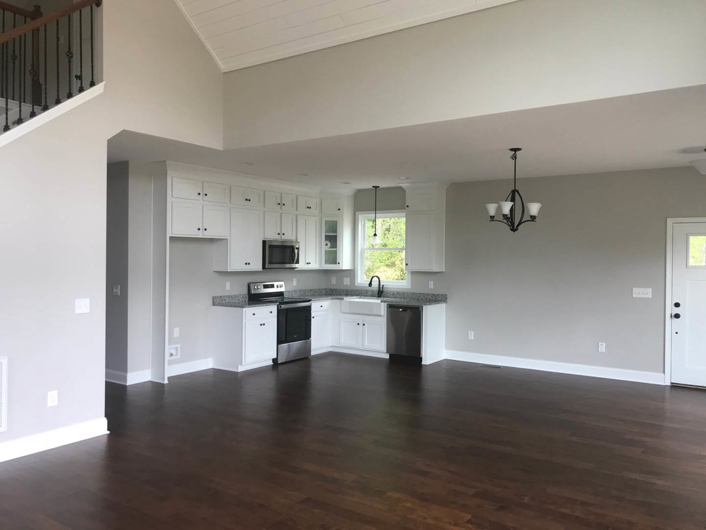 Open kitchen and dining area with dark hardwood floors, white walls, wood cabinetry, stainless steel appliances, and a modern chandelier above the dining table.