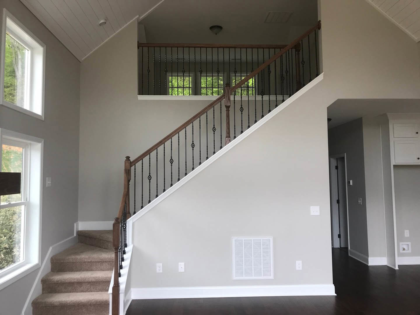 Wood staircase with black metal railings, white walls, vent near base, and window overlooking green field