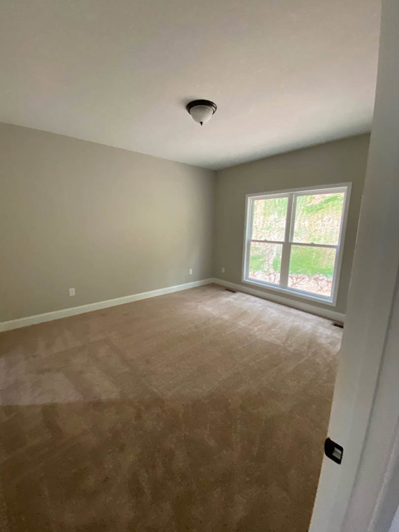 Carpeted room with white walls, large window overlooking green lawn, ceiling fan, and recessed lighting