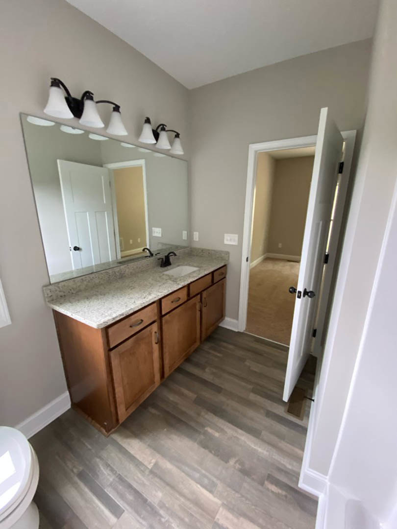 Bathroom with marble countertop, rectangular mirror above sink, white cabinetry, chrome faucet, and wall-mounted light fixtures
