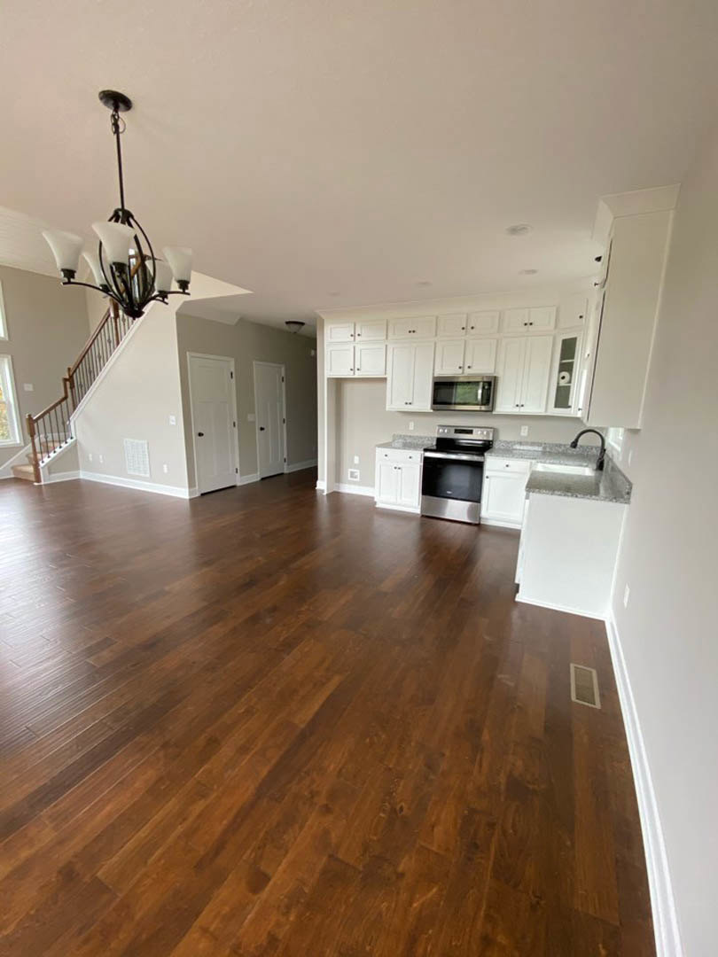 Open kitchen and dining area featuring wide-plank hardwood floors, white cabinetry, stainless steel appliances, and a modern chandelier above a wooden dining table.