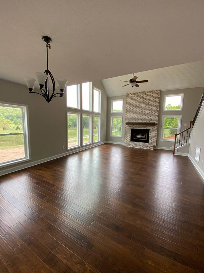 Spacious living room featuring hardwood floors, brick fireplace, chandelier, and ceiling fan with light fixture.